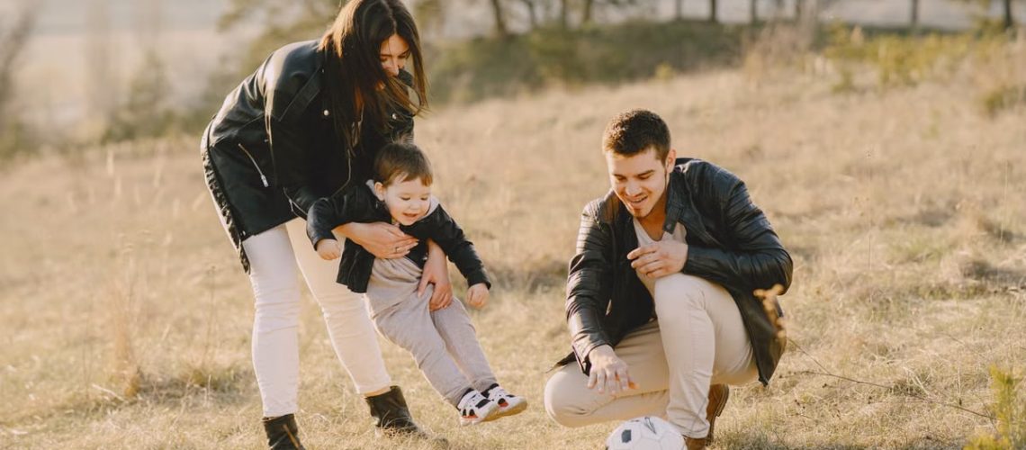 A happy family playing with a soccer ball in a grassy field on a sunny day.