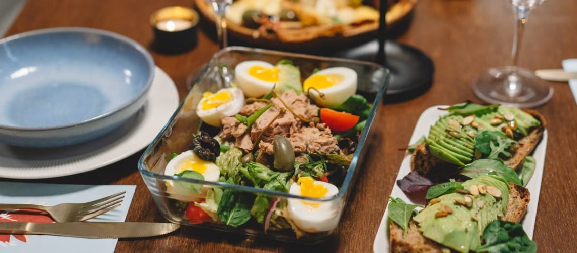 Elegant dining setup with fresh salad, avocado toast, and wine glasses on a wooden table.